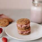 Close-up of raspberry ice cream sandwiches stacked on a plate beside fresh raspberries.